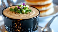 Creamy mushroom soup garnished with fresh herbs and black pepper in dark ceramic bowl, served with bagels. Homemade comfort food with rich texture.
