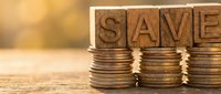 Stacks of coins with wooden letter blocks spelling SAVE on warm wooden surface representing financial savings and money management concepts.