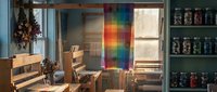 Cozy kitchen interior with rainbow light prism streaming through window onto wooden table and chairs, creating colorful spectrum on wall with jars on shelves.