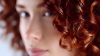 Young Asian woman with vibrant copper red curly hair and natural makeup in soft focus close-up portrait showing modern beauty and hair styling trends.