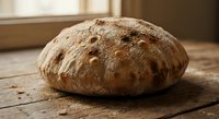 Freshly baked artisan sourdough bread loaf with rustic crust on wooden surface near window. Homemade bakery product for cooking and food photography.