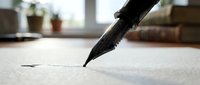 Close-up of black fountain pen writing on white paper with blurred home interior background. Business correspondence and creative writing concept.