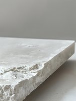 Rough edge of white marble slab against neutral background showcases natural stone texture and raw architectural material detail for luxury interior design.