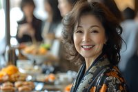 Elegant mature Asian woman with radiant smile wearing traditional floral kimono at upscale restaurant buffet, expressing joy and confidence during social gathering.