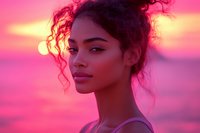 Young woman with curly hair in messy bun gazing into distance against vibrant pink and purple sunset sky, profile portrait capturing natural beauty and confidence.