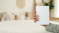 Woman holding blank white card in modern home interior with neutral decor, suitable for mockups, advertising, and promotional designs.