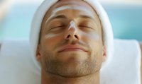 Young man with white headband relaxing during spa treatment with eyes closed, expressing tranquility and wellness against soft blue background.