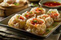 Steamed Asian dumplings with spicy chili sauce garnished with green onions and sesame seeds served on metal tray, close up view of traditional dim sum.