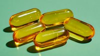 Transparent amber fish oil capsules on mint green background, showcasing omega-3 supplements for health and wellness benefits.