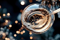 Overhead view of swirling coffee or espresso in glass cup with spoon, bubbles and foam creating dynamic motion against blurred bokeh background for beverage and lifestyle content.