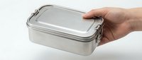 Caucasian hand holding a stainless steel lunch box with metal clasps on white background, eco-friendly reusable food container.