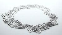 Silver metal paper clips arranged in circular chain formation on white background for office supplies and business concepts.