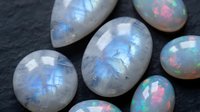 Luminous rainbow moonstone gemstones displaying iridescent blue and multicolor flashes on dark slate surface for jewelry making and crystal healing.