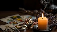 Mystical fortune telling scene with burning candle, crystal ball and tarot cards on wooden table creating atmospheric divination setting.