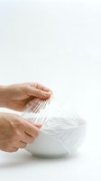 Hands of adult male removing transparent plastic wrap from white bowl on isolated background, food storage and kitchen preparation concept.