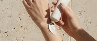 Two hands holding white product on sandy beige surface with natural shadow, cosmetics mockup for skincare branding and packaging design.