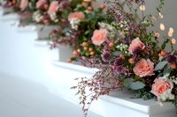 Romantic floral arrangement with soft pink roses and delicate purple wildflowers on white surface, featuring blurred bokeh lights and eucalyptus greenery. Perfect for weddings.