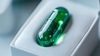 Green capsule with glowing particles and sparkles on white surface, suitable for pharmaceutical, wellness, supplement, and medical advertising campaigns.