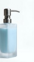 Glass soap dispenser with blue liquid and silver pump on white background, isolated for hygiene, bathroom, and skincare product concepts.