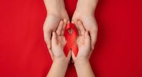 Hands holding red ribbon symbol for HIV AIDS awareness, healthcare support and solidarity campaign on red background for medical education and prevention.