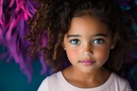 Young mixed race girl with bright blue eyes and curly hair against colorful abstract background, wearing pink shirt. Close up portrait showing natural beauty and innocence.