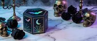 Mystical hexagonal box with celestial moon and star symbols surrounded by black roses, skulls and candles on marble surface for gothic witchcraft themes.