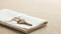 Brass key with keyring resting on folded white cloth napkin against neutral beige linen background, symbolizing security, access, and property ownership for design projects.