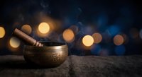Tibetan singing bowl with wooden mallet on textured surface against bokeh lights background for meditation, sound therapy and spiritual wellness practices.