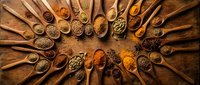 Wooden spoons filled with colorful spices and herbs arranged in circular pattern on rustic wood background for culinary cooking and seasoning applications.