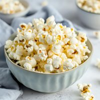 Fresh popcorn served in light blue ceramic bowl on white marble surface with soft gray linen napkin, perfect for movie night snack photography.