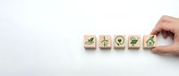 Hand placing wooden blocks with green eco-friendly icons including checkmark, wind turbine, recycling, leaf and house on white background for sustainability concepts.