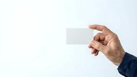 Male hand in dark blue sleeve holding blank white business card against neutral background for corporate branding and contact information display.