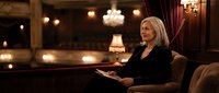 Elegant mature blonde businesswoman reading documents in luxury hotel lobby with warm lighting and classic interior design for corporate lifestyle.