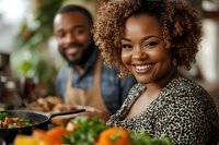 Happy African American woman with curly hair smiling while cooking with partner in modern kitchen. Couple preparing healthy meal together at home.