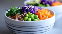 Fresh poke bowl with raw tuna, edamame beans, shredded carrots, purple cabbage and green onions in striped ceramic bowl. Asian fusion cuisine.