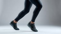 Athletic legs in black leggings and sneakers running on gray background. Fitness workout concept for sports training and healthy lifestyle.