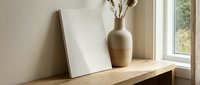 Blank canvas mockup leaning on wooden shelf beside ceramic vase with dried flowers near window, minimal Scandinavian interior design.