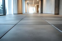 Modern office corridor with gray tile flooring, low angle perspective focusing on floor texture, illuminated by ceiling lights creating depth and leading lines.