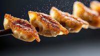 Pan-fried Asian dumplings with crispy golden crust on dark background with steam and flying spices, close up view of traditional potstickers or gyoza.