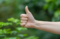 Hand showing thumbs up gesture against blurred green nature background. Positive approval sign for success and achievement concepts.
