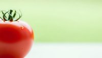 Fresh red tomato with green stem on light background for healthy cooking and organic food concepts.