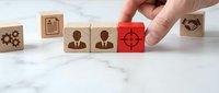 Hand selecting red target block from wooden business cubes representing strategic planning and goal achievement in corporate management concepts.