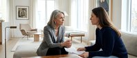 Professional mature businesswoman mentor coaching young female employee during office meeting discussing career development and workplace guidance.