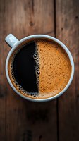 Fresh brewed coffee in white ceramic cup with rich crema and dark foam bubbles, viewed from above on rustic wooden background. Perfect for food blogs.