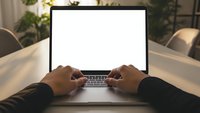Hands typing on laptop with blank white screen in modern office workspace, mockup template for presentations and digital content creation.