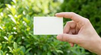Hand holding blank white business card mockup against green nature background for branding and corporate identity design projects.
