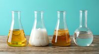 Laboratory glassware with colorful chemical solutions on wooden table against turquoise background for scientific research and education.