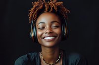 Young African American woman with dreadlocks and wireless headphones smiling with eyes closed, expressing joy and relaxation against dark background.