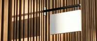 Modern black floor lamp with white drum shade against wooden slat wall creating geometric shadow patterns in contemporary interior design setting.