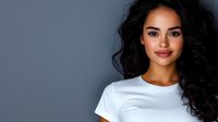 Young mixed race woman with long dark curly hair and bright smile wearing white t-shirt against gray background, looking confident and friendly. Professional portrait.